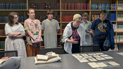 Six people standing up around a table and observing some Collections items