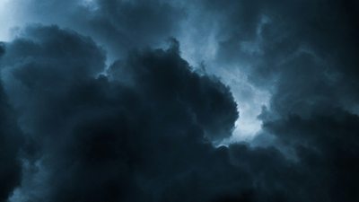 Dark grey clouds cover up a dim blue sky. Some light pokes through the mass of clouds