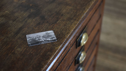 Card that says Royal Geographical Society placed on tob of an old wooden chest of drawers.