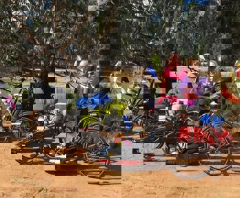 Two cyclists, one with a hand cycle, pose for a photo by a lake in a dry landscape.