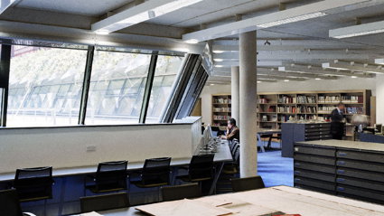 One person sits before a computer whilst the other looks at books on a shelf in in the Foyle reading room.