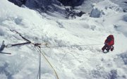 An expeditioner holding on to a rope into a deep open crack in a glacier.