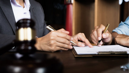 Close-up of two pairs of hands, one holding a fountain pen, the other pointing at a paper for signing.