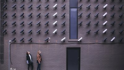 Lots of surveliance cameras on a wall looking at two people