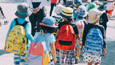 Children walk acrros the road in pairs whilst holding hands. A teacher wals besides them for their safety