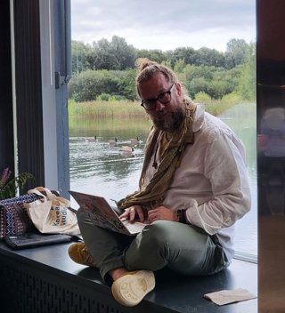 Niki Alsford sitting with a laptop next to a window that overlooks a pond.