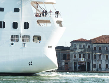 A cruise ship moves close to old homes along a Venetian canal.