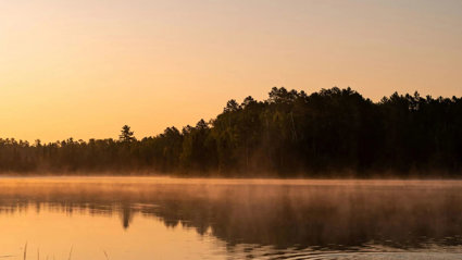Sunset behind a lake, with trees on the bank of the lake.