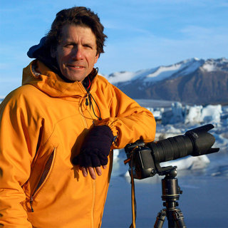 James Balog in an arctic region leaning on a camera perched on a tripod.