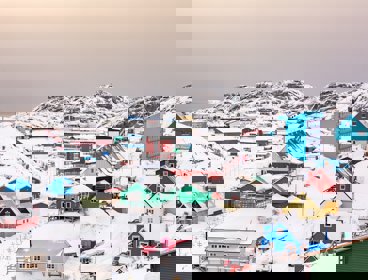 A view over a town in Greenland with colourful housing and snow covered ground and mountains