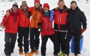 Six expeditioners in winter gear gleefully posing for a photo while standing in a snow covered landscape.