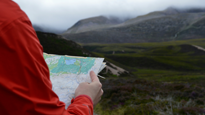 Person looks at map whilst standing in the the Scottish Highlands.