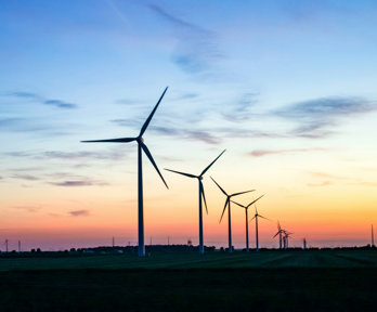 Wind turbines in shadow with sunset background.