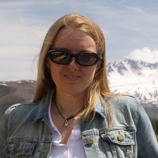 Person wearing sunglasses with blonde hair against mountain background.