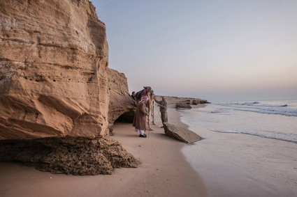 Coastal cliff with sandy beach- people and a camel are standing near the cliff bottom