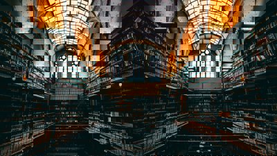 A dark, historic library with towering shelves and an arched glass ceiling.