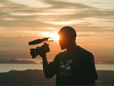 Person holding camera against sunset background.