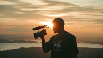 Person holding camera against sunset background.
