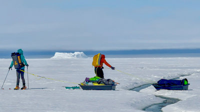Two researchers pulling sleds on a large ice sheet.