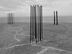 Black and white photograph showing a barren space and three distinct structures 