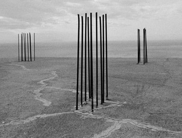 Black and white photograph showing a barren space and three distinct structures