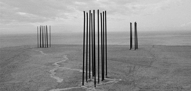 Black and white photograph showing a barren space and three distinct structures