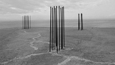 Black and white photograph showing a barren space and three distinct structures
