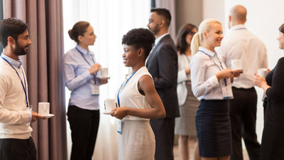 Business people with conference badges and coffee chatting with each other in a brightly lit room.