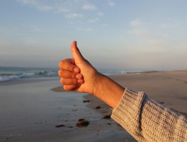 Hand with thumb up against beach background.