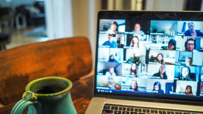 A cup next to a laptop with a blurry screen showing different people who are in an online meeting. 