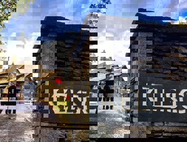 Two people walking towards a stone building with a gate post.