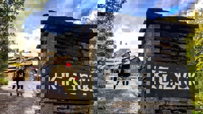 Two people walking towards a stone building with a gate post.