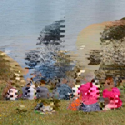 A group of people on a cliff edge by the sea, doing a field sketch of the view of cliffs and bay