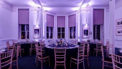 Round dinner tables set-up in the Education Centre with purple uplighters. 