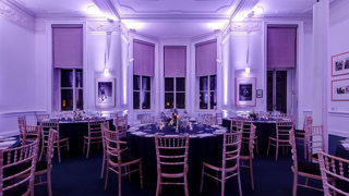 Round dinner tables set-up in the Education Centre with purple uplighters. 