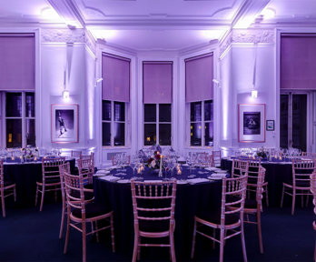 Round dinner tables set-up in the Education Centre with purple uplighters. 