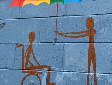 A mural artwork showing a wheelchair user and a person holding an umbrella above their head