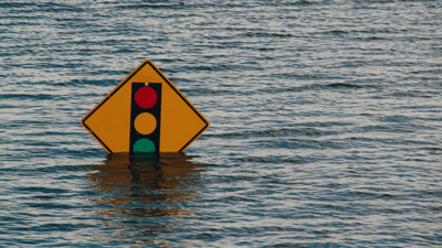 A traffic sign stands submerged in flood waters. the poll holding up the sign is completely submerged. 