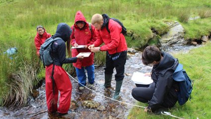 Group of young people standing in stream conducting fieldwork.