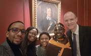 Five people smiling for selfie in front of old picture.  