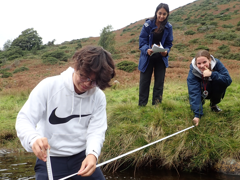 Three pupils on a fieldtrip measuring the depth of the River Caldew in Cumbria.