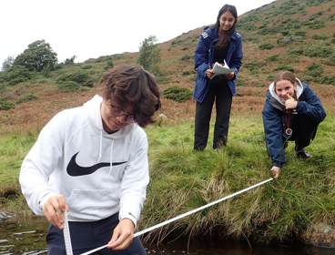 Three pupils on a fieldtrip measuring the depth of the River Caldew in Cumbria.