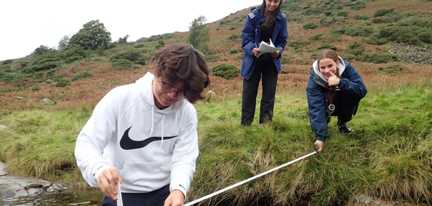 Three pupils on a fieldtrip measuring the depth of the River Caldew in Cumbria.