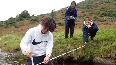 Three pupils on a fieldtrip measuring the depth of the River Caldew in Cumbria.