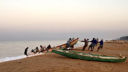 Group of people on a beach pulling a rowing boat onto the shore from the water.