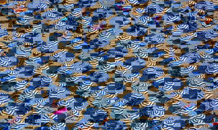 An aerial view of blue and white parasols and sun loungers on a sandy beach
