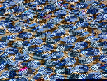 An aerial view of blue and white parasols and sun loungers on a sandy beach