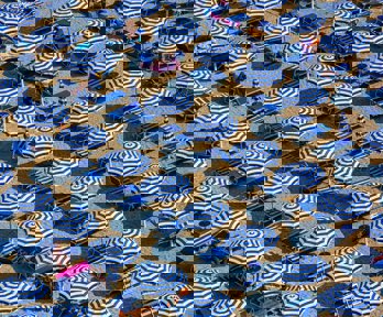 An aerial view of blue and white parasols and sun loungers on a sandy beach