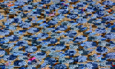 An aerial view of blue and white parasols and sun loungers on a sandy beach