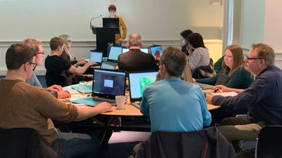 A group of teachers sit around a table with their laptops. They are using ArcGIS.